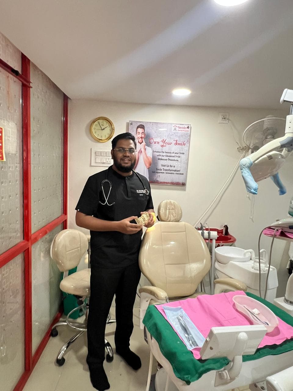 Dr. Md. Miftah Ur Rahman, Prosthodontist and Implantologist, standing beside the dental chair in a treatment room at NeoDent Dental Hospital, Hyderabad, holding a dental study model